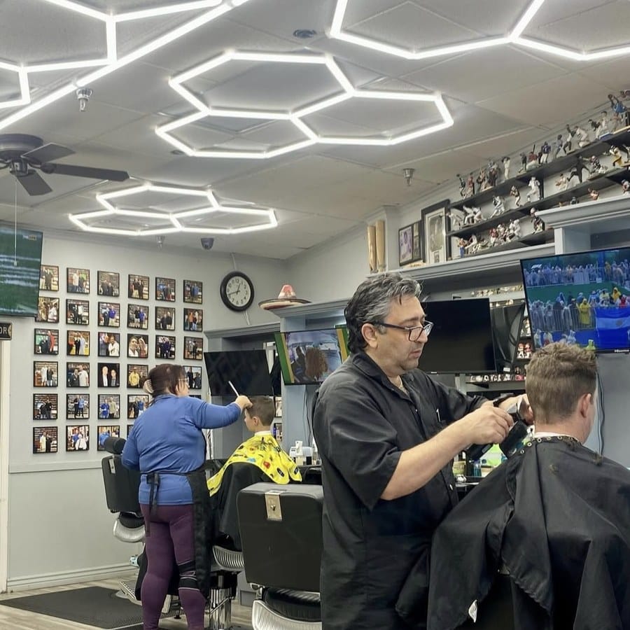 Master barber Phil Malayev cutting a client's hair at The Pavilions Barbershop in Scottsdale, with a memorabilia wall and vintage chairs in the background